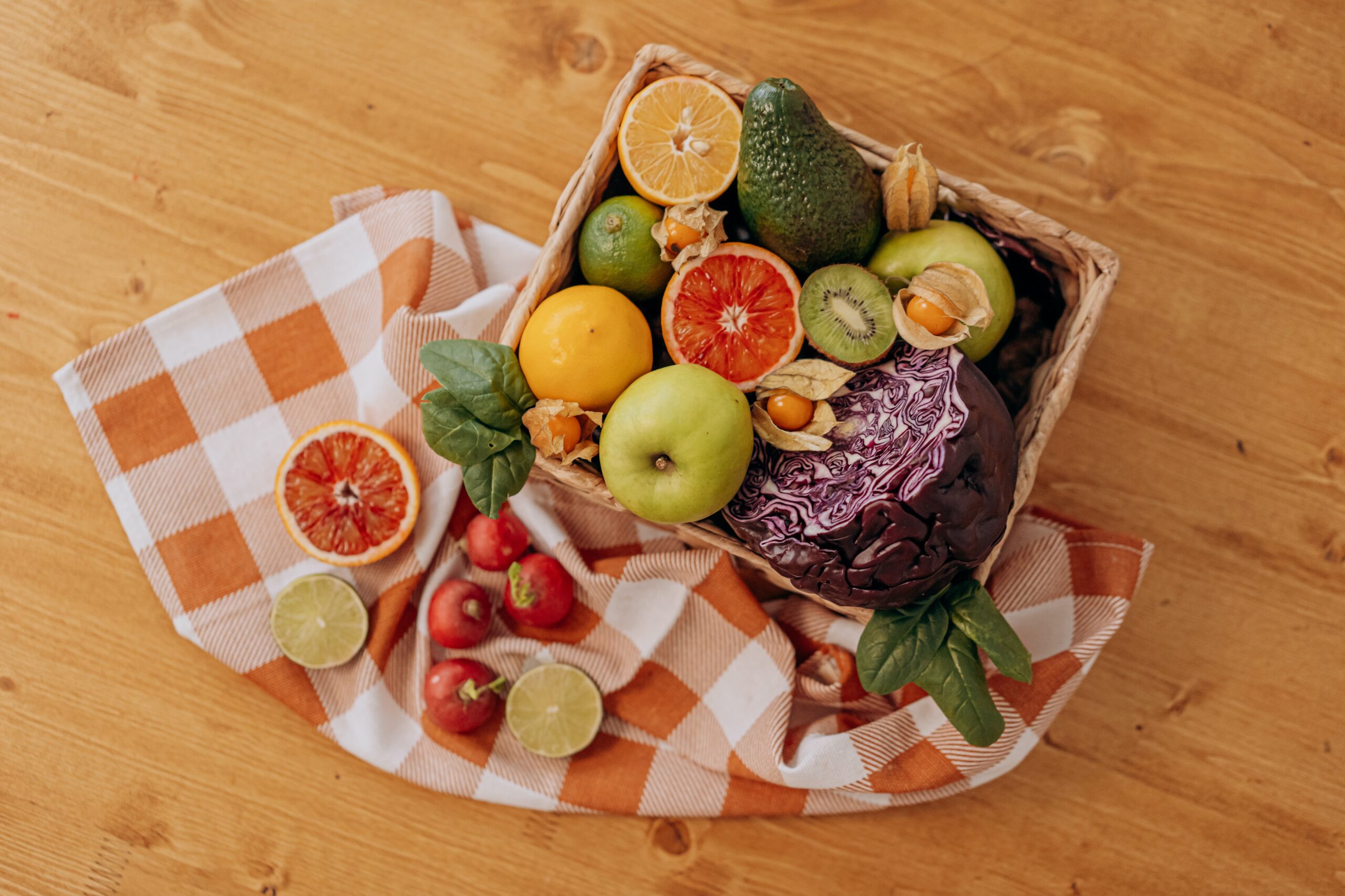 A fruit and vegetable wooden basket and an orange and white chequered picnic cloth with wooden background.