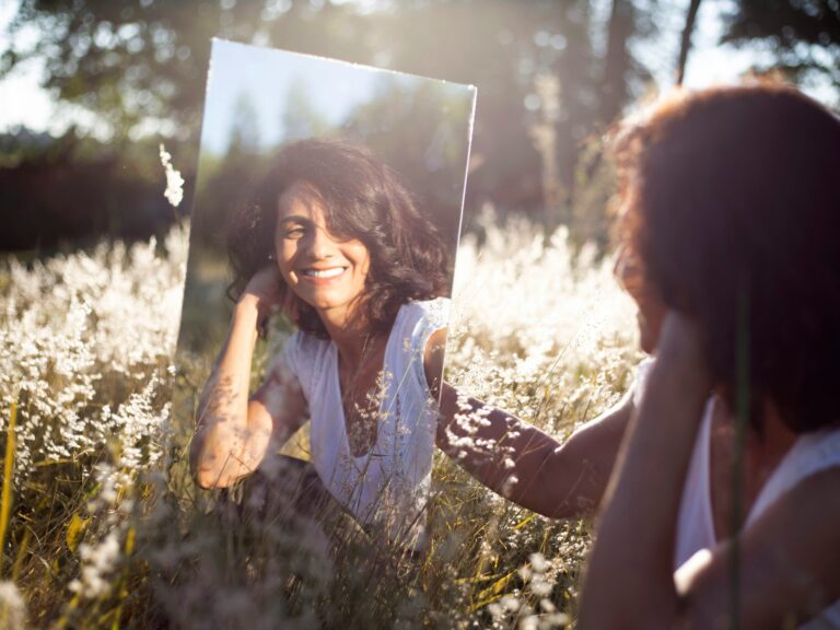 A women smiling a holding a mirror in a sunny flower field.